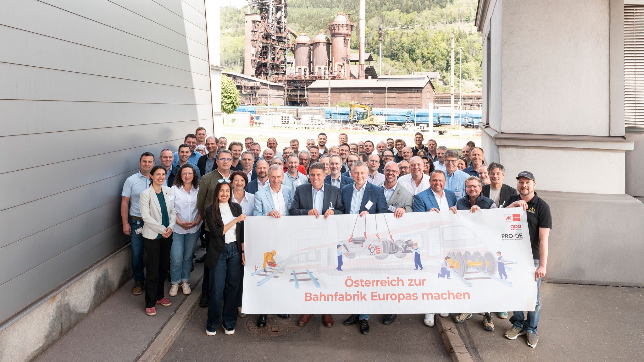 Die Teilnehmer:innen der Konferenz im Werk Donawitz der voestalpine mit Transparent "Österreich zur Bahnfabrik Europas machen"