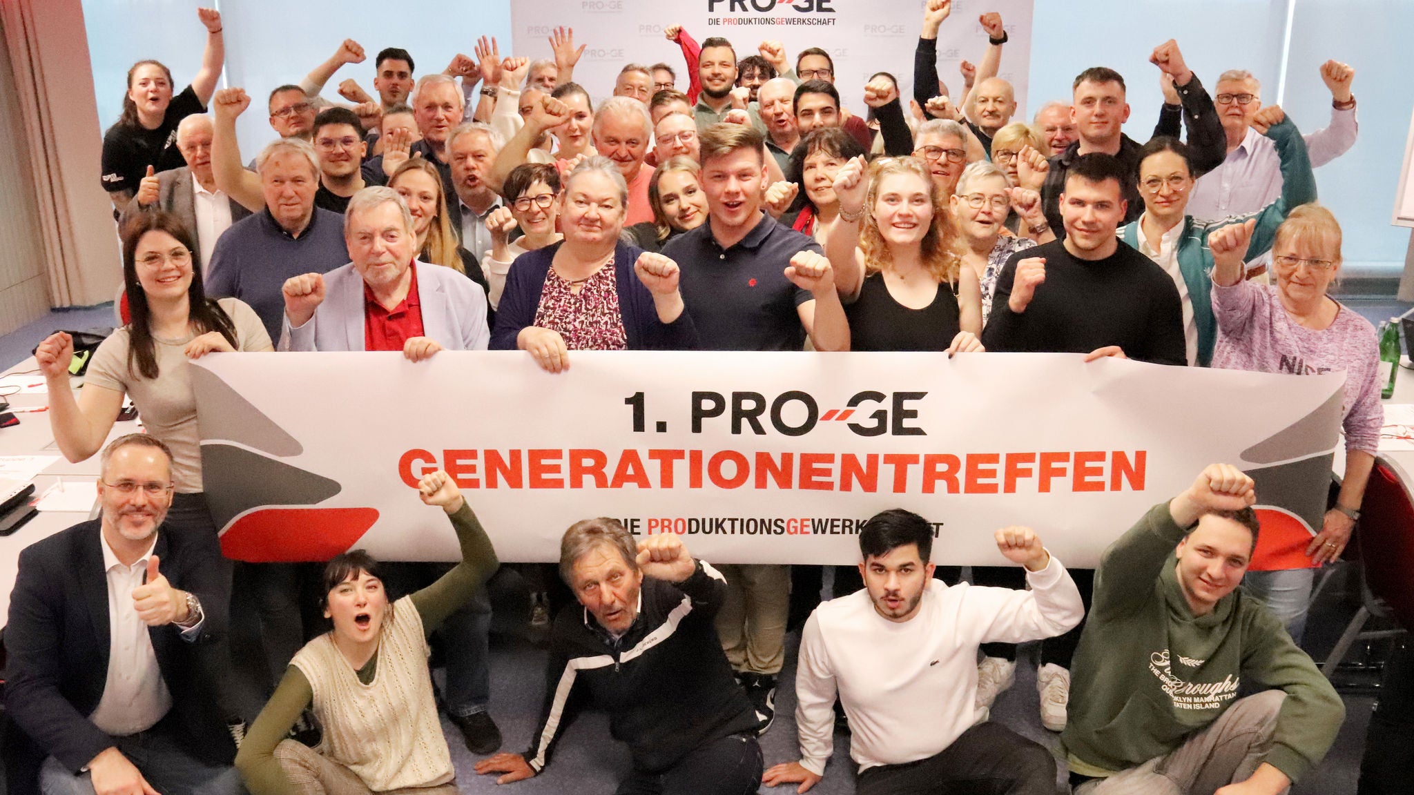 Gruppenfoto von zahlreichen jungen und älteren Menschen, die ein Transparent mit der Aufschrift "1. PRO-GE Generationentreffen" halten.