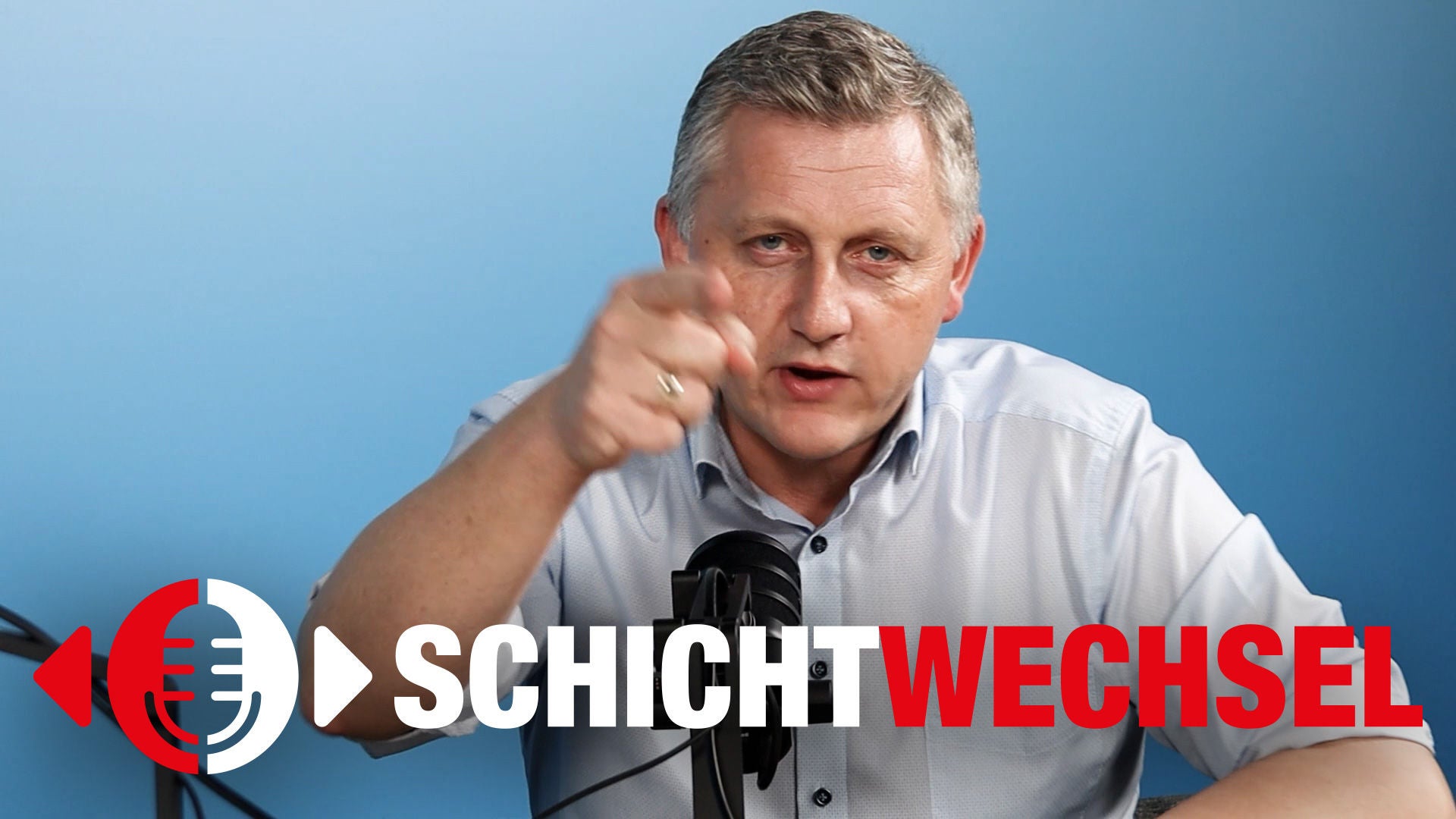 Reinhold Binder vor hellblauem Hintergrund, Blick in die Kamera, Hand gehoben zeigt mit dem Finger ebenfalls in die Kamera, Podcast-Logo SCHICHTWECHSEL
