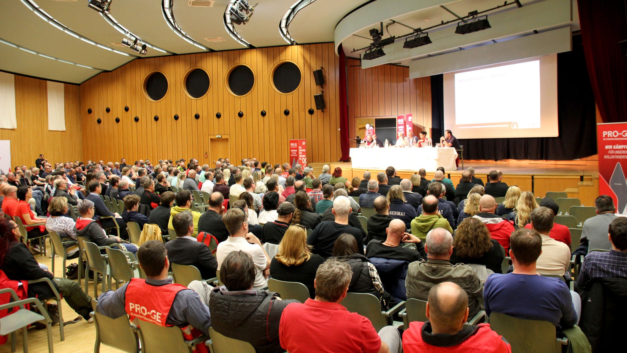 Konferenzsaal mit Teilnehmer:innen, Blickrichtung auf Podium