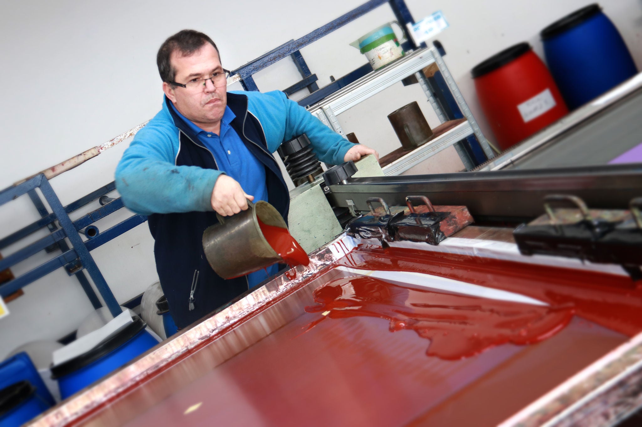 Mann gießt rote Farbe in eine Siebdruckmaschine