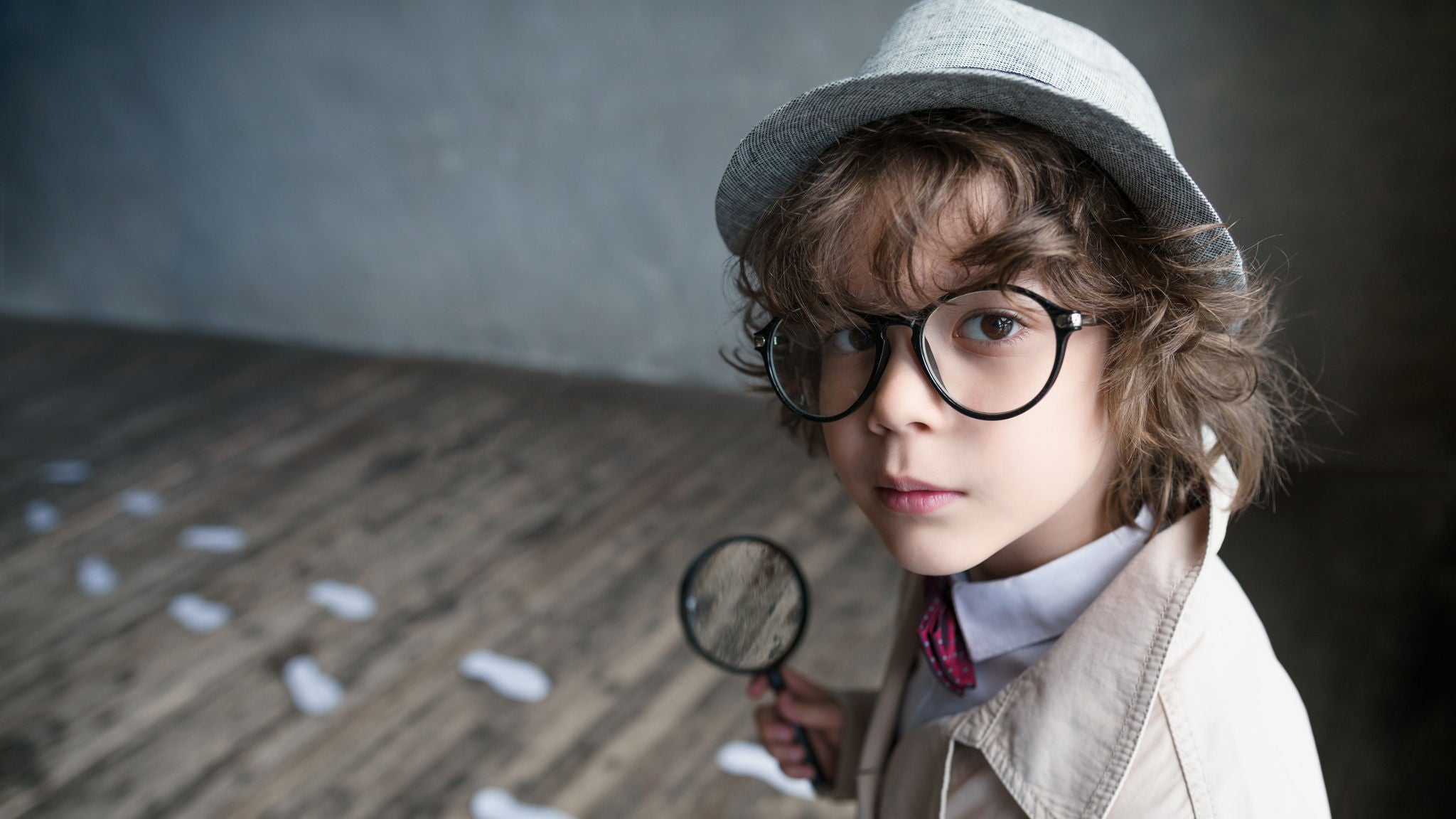 Kind mit Sherlock Holmes Kleidung und Lupe und Fußspuren am Boden