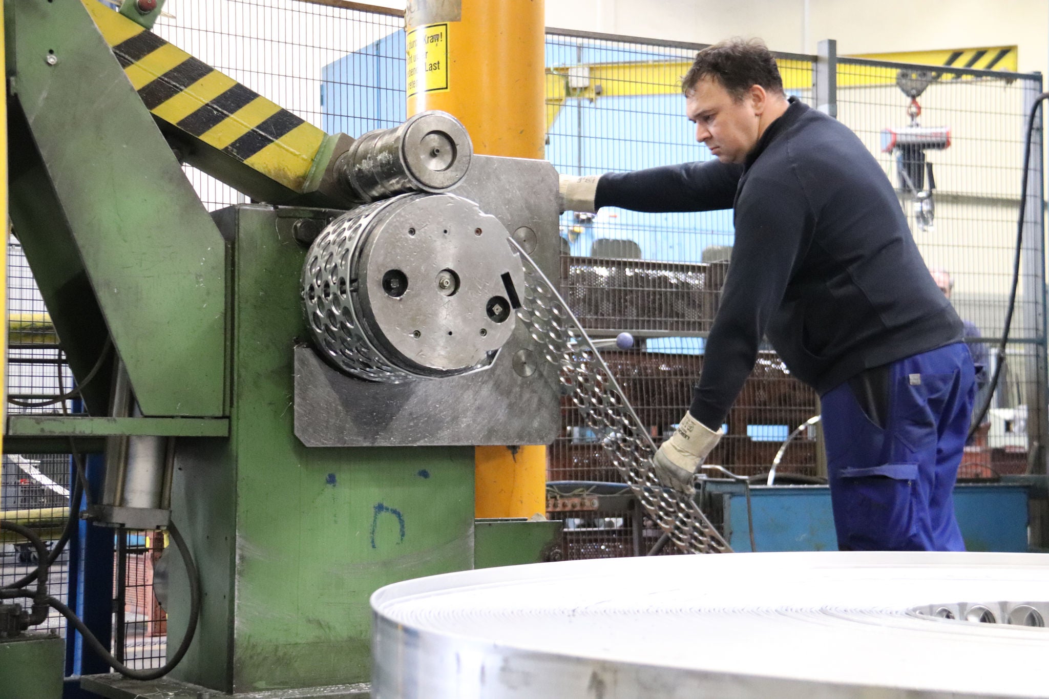 Arbeiter steht an einer Maschine, die das Aluminiumband mit den ausgestanzten Butzen aufwickelt.