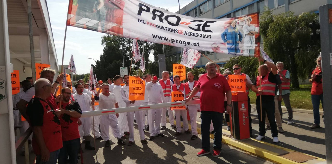 Mehrere Menschen stehen vor der Werkseinfahrt zur Firma Ardo mit einem großen Transparent der PRO-GE und Plakaten mit der Aufschrift "Hier wird gestreikt".