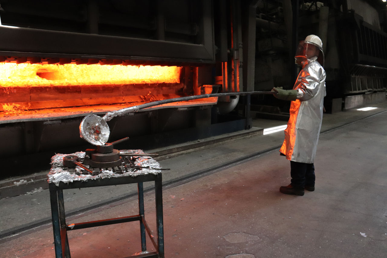 Ein Arbeiter im Hitze-Anzug nimmt eine Probe von flüssigem Aluminium aus dem Hochofen.